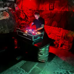 DJ miksuje muzykę na sprzęcie Shure, podświetlonym czerwonym światłem, na tle kamiennej ściany w klubie.