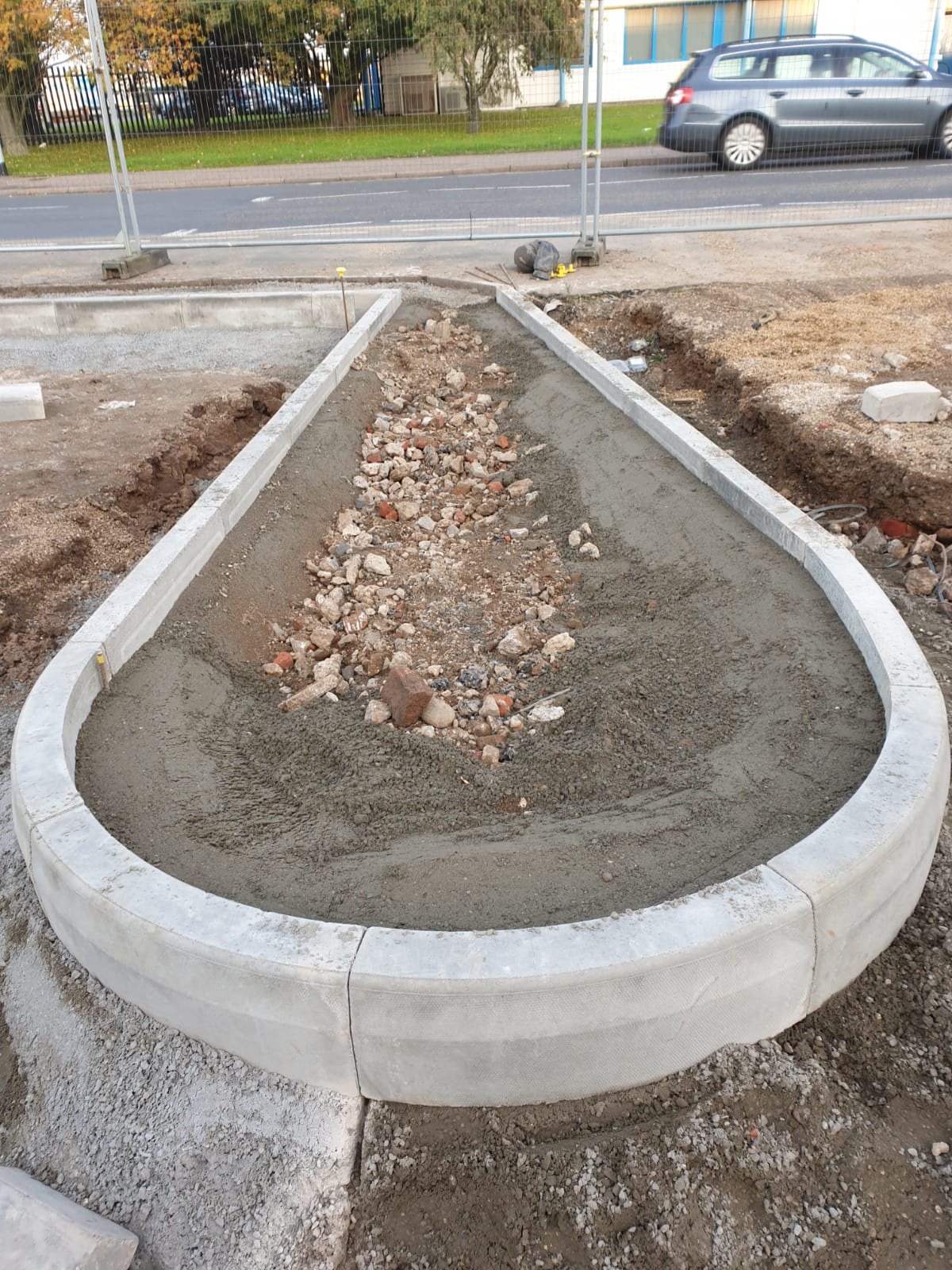 Przygotowanie podłoża pod ścieżkę z obrzeżami betonowymi, wypełnioną gruzem i piaskiem, widok z góry, w tle ulica i samochód.