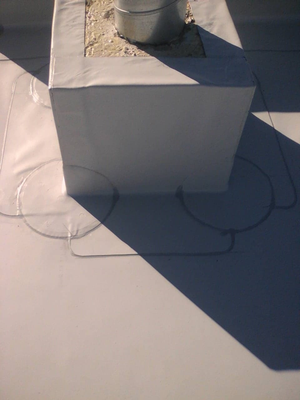 Szczelne obłożenie komina na płaskim dachu z widocznymi okrągłymi uszczelnieniami wokół rur wentylacyjnych, zabezpieczone białą membraną dachową.