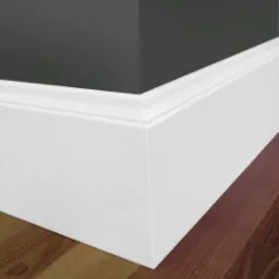 Szczegółowe ujęcie narożnika ściany pomalowanej na ciemny grafit, z białą listwą przypodłogową o profilowanym kształcie, na tle parkietu z naturalnego drewna.