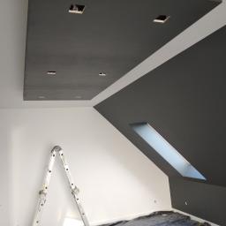 Art-Clean - Pomieszczenie w trakcie malowania: sufit i ściana pomalowane na ciemny grafit, białe ściany, drabina aluminiowa, zabezpieczona podłoga folią, otwory na oświetlenie w suficie.