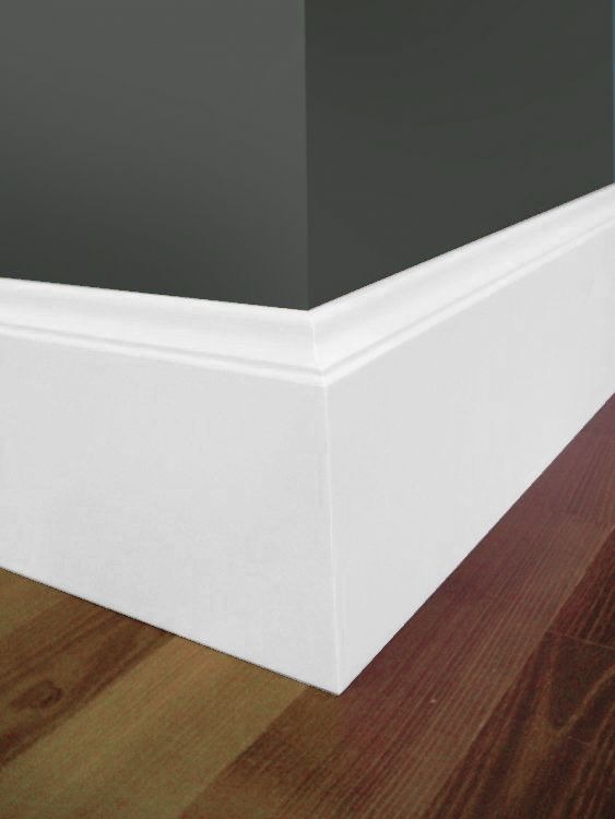 Szczegółowe ujęcie narożnika ściany pomalowanej na ciemny grafit, z białą listwą przypodłogową o profilowanym kształcie, na tle parkietu z naturalnego drewna.