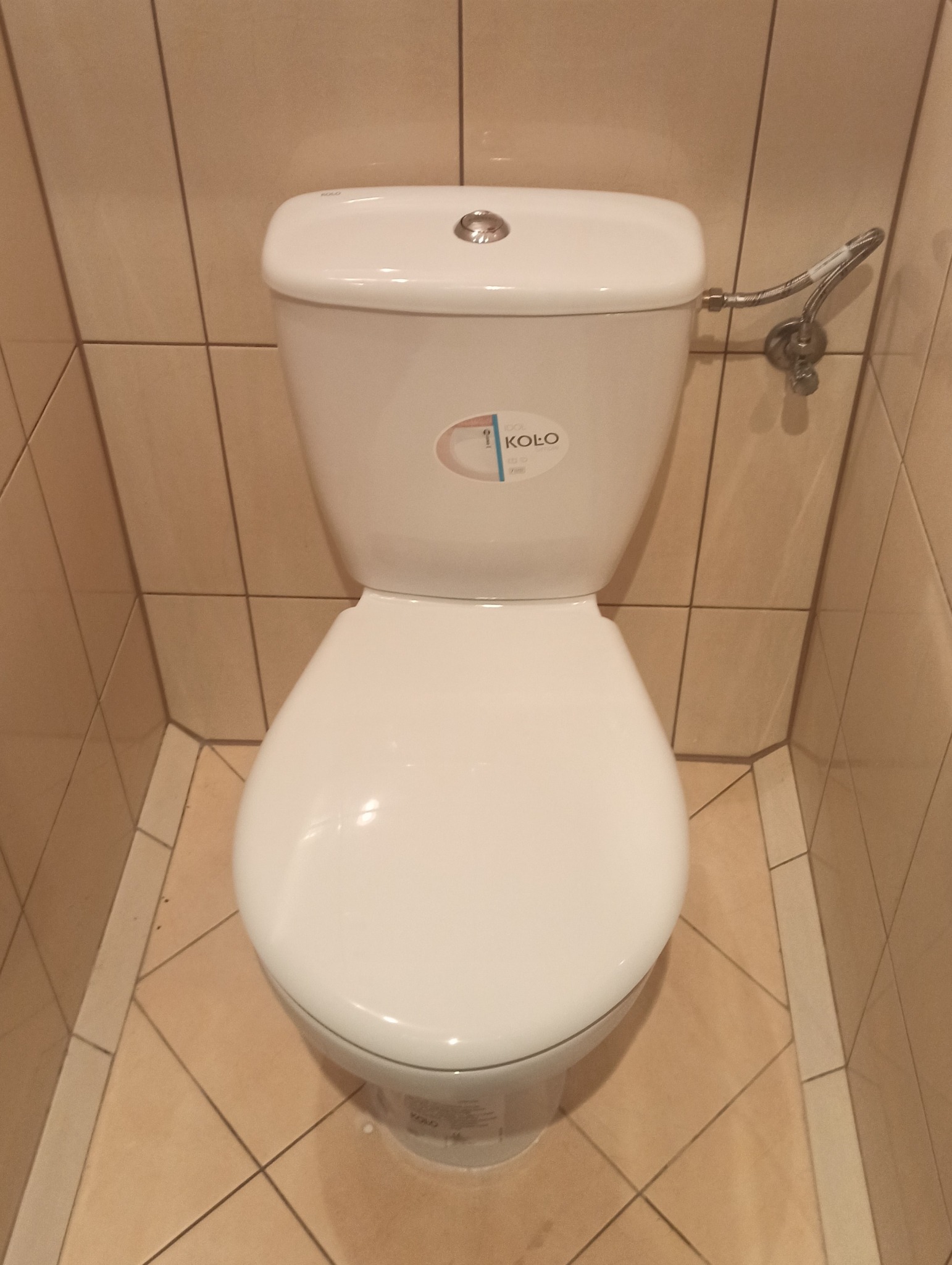 Kompakt WC marki Koło, widok z góry, z widocznym przyłączem wodnym i beżowymi płytkami w tle.