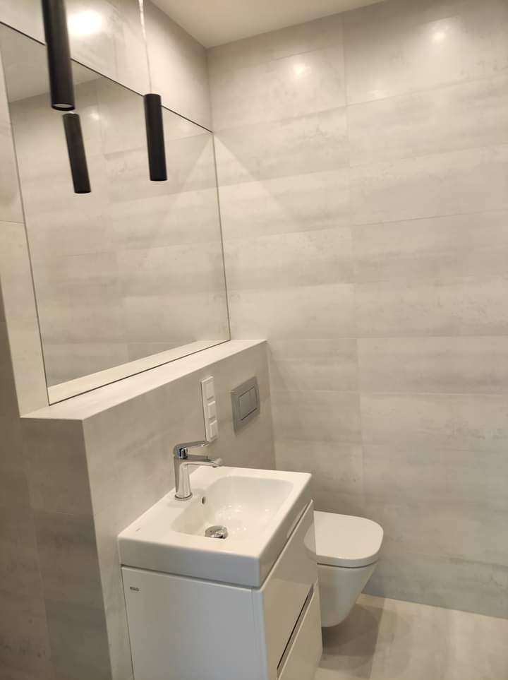 Nowoczesna łazienka w odcieniach szarości z wiszącą toaletą, umywalką z szafką i minimalistycznym oświetleniem