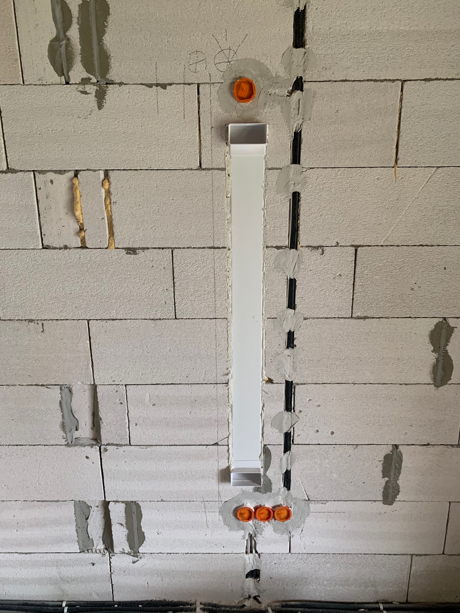 Instalacja elektryczna w ścianie z betonu komórkowego: widoczne rury osłonowe, puszki instalacyjne z pomarańczowymi pokrywkami oraz biała listwa maskująca przewody.