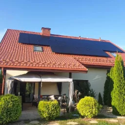 Dom jednorodzinny z panelami słonecznymi na czerwonym dachu, widok z ogrodu w słoneczny dzień.