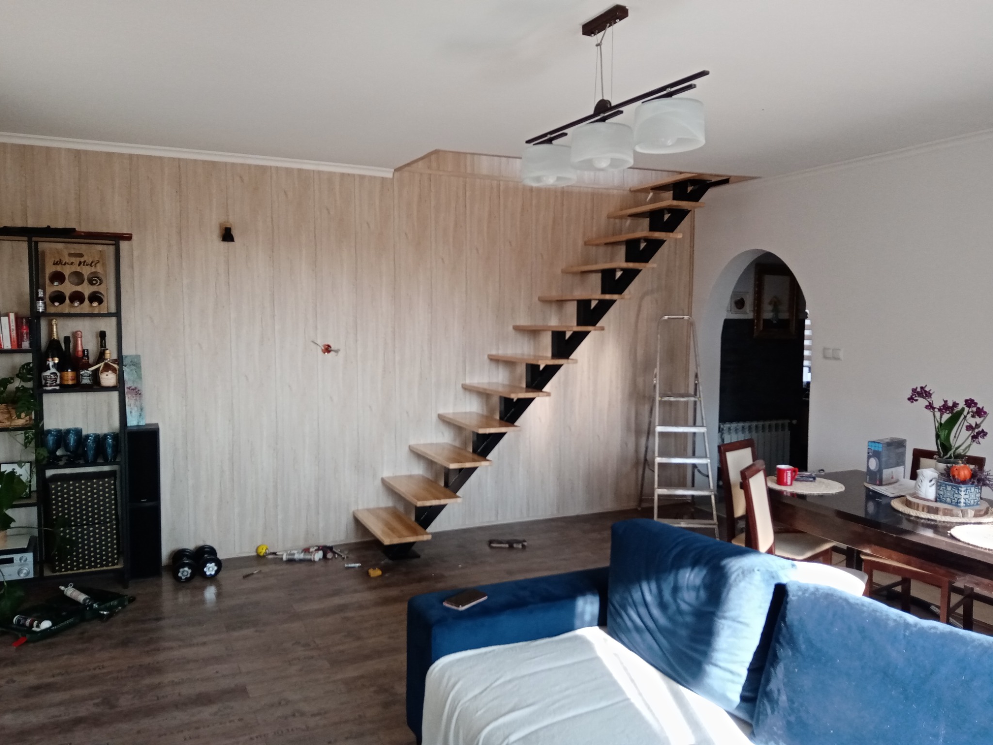 Nowoczesne schody z drewnianymi stopniami i metalową konstrukcją w jasnym wnętrzu domu, widoczne narzędzia na podłodze sugerują trwający montaż.