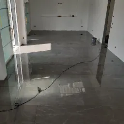 Położona, błyszcząca, szara glazura imitująca marmur w pomieszczeniu w Koninie, widoczne przygotowania do dalszych prac wykończeniowych.