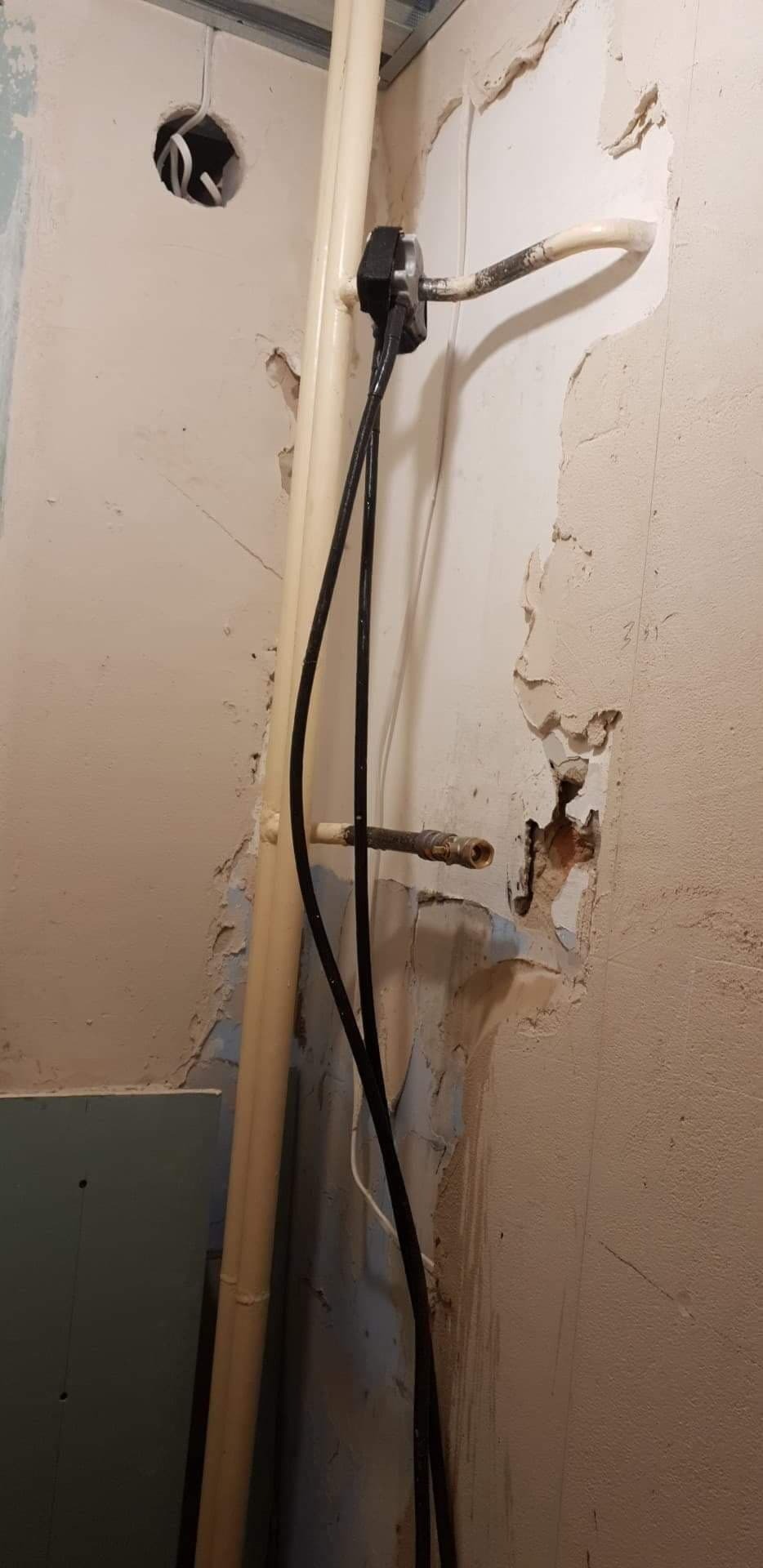 Fragment ściany w trakcie prac instalacyjnych: widoczne rury, przewody elektryczne, uszkodzony tynk i otwór w suficie pod instalacje.
