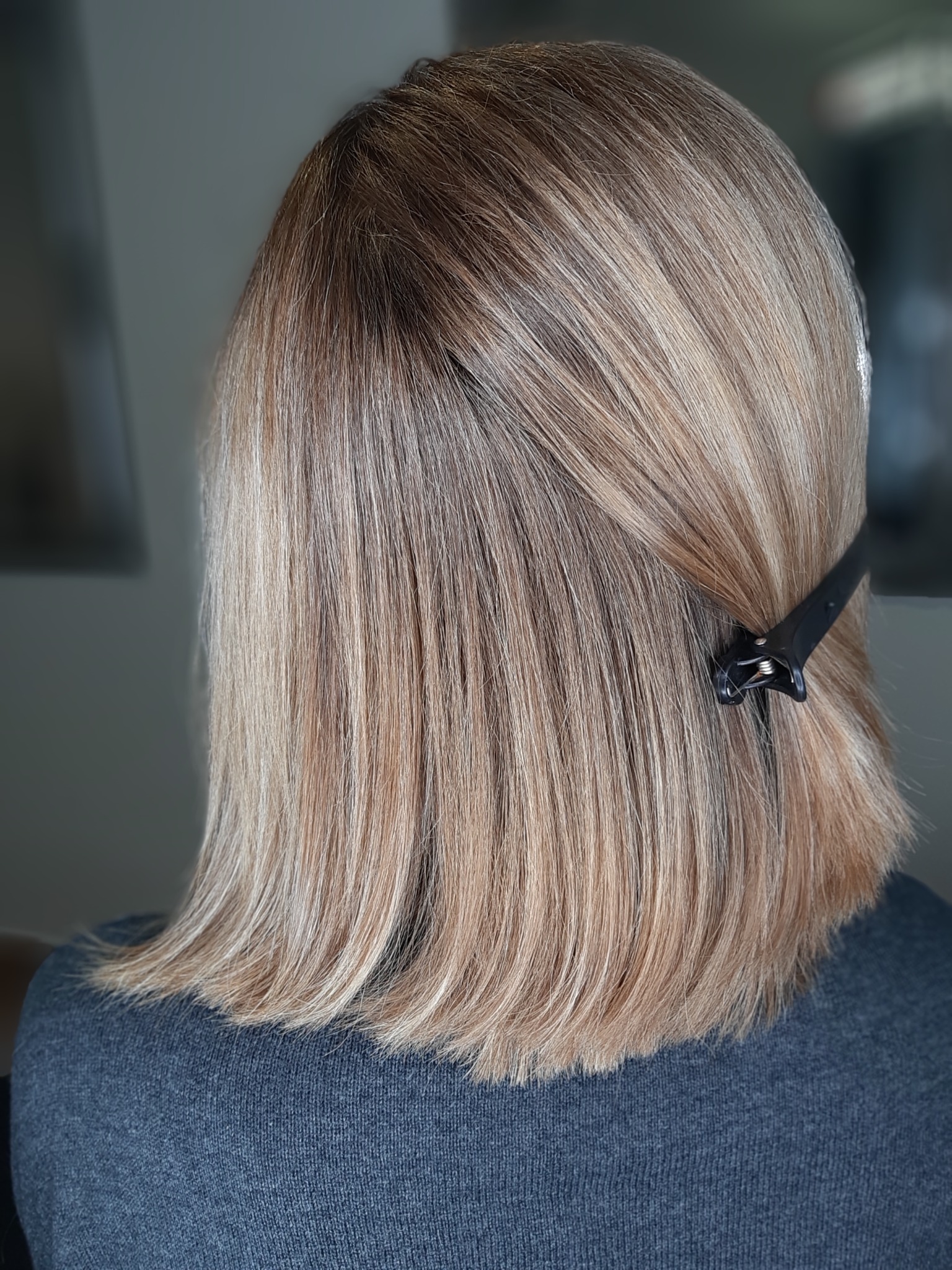 Blond włosy z brązowymi odrostami, upięte czarną klamrą, widok z tyłu, końcówki podwinięte do wewnątrz.