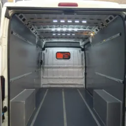 Wnętrze pustej furgonetki z zamontowanymi szynami mocującymi i oświetleniem LED w suficie, przygotowanej do transportu towarów.