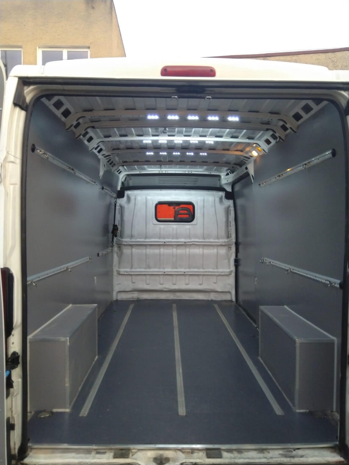 Wnętrze pustej furgonetki z zamontowanymi szynami mocującymi i oświetleniem LED w suficie, przygotowanej do transportu towarów.