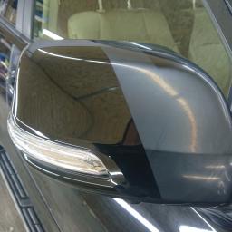 SteamWash Dawid Karpicki - Błyszczące, czarne lusterko boczne samochodu po detailingowym polerowaniu, widoczny wyraźny kontrast między obszarem po zabiegu a obszarem przed, zarys wnętrza pojazdu w tle.