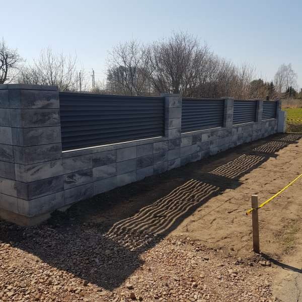 Nowoczesne ogrodzenie z szarej cegły łupanej i poziomych paneli w kolorze grafitowym, widok z poziomu gruntu, zarysowane cienie na piasku.