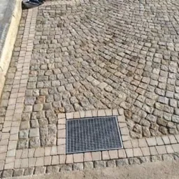 Ułożona nawierzchnia z kostki granitowej w kształcie wachlarza, obrzeża z mniejszej kostki, kratka ściekowa wkomponowana w powierzchnię.