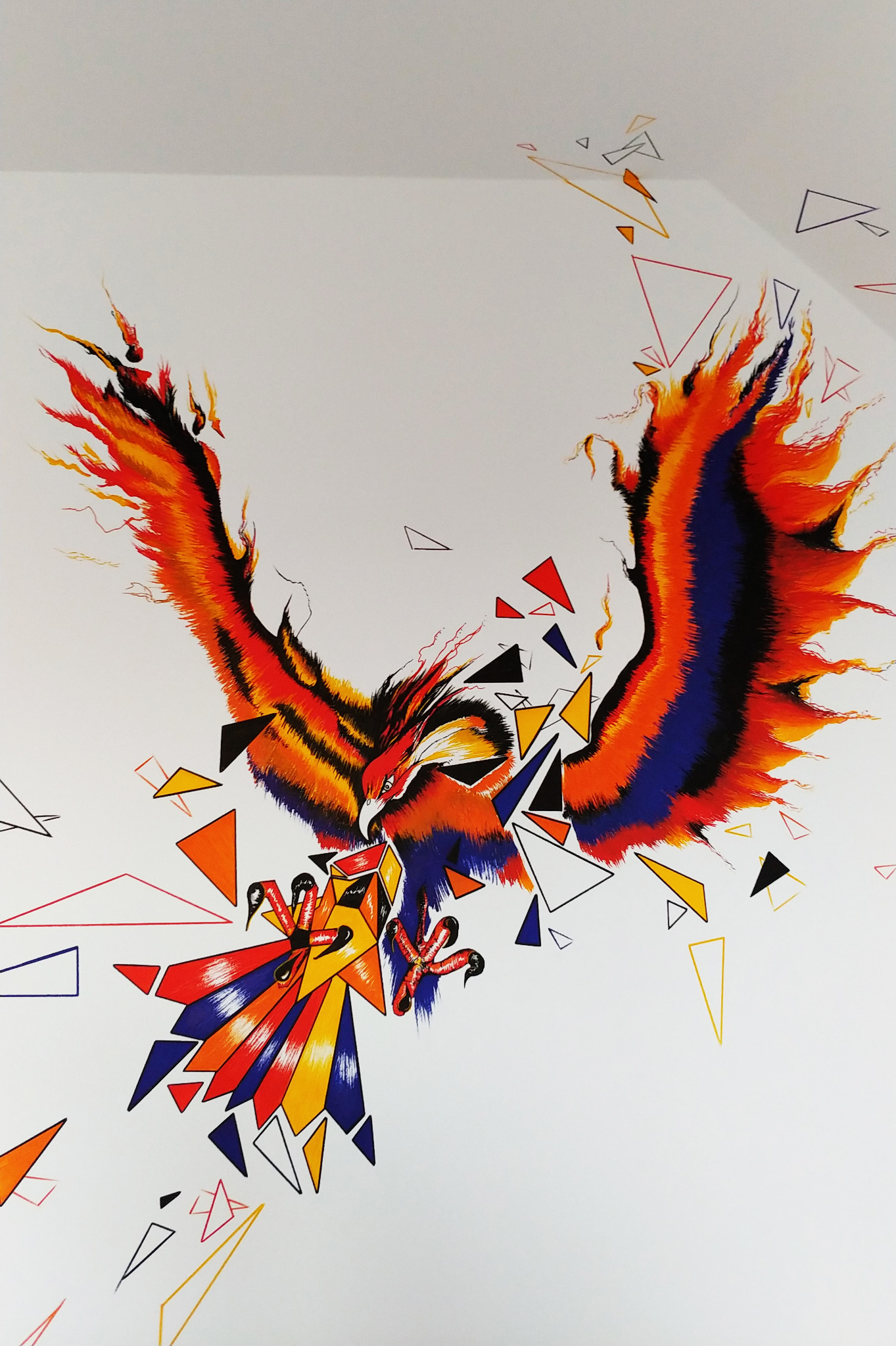 Ilustracja malarska przedstawiająca geometrycznego feniksa w locie, z pomarańczowo-czerwonymi skrzydłami i geometrycznymi elementami w kolorach czerwonym, niebieskim i żółtym na białym tle.