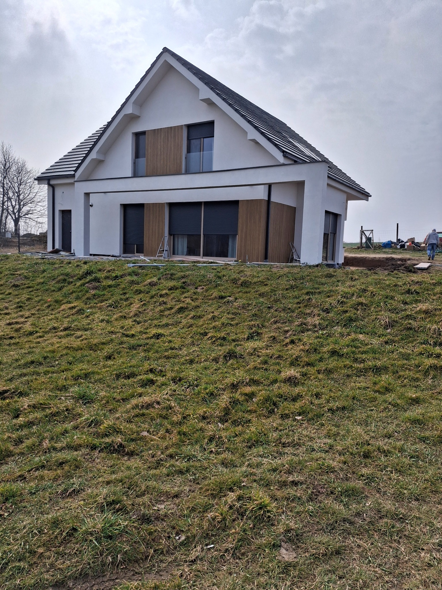 Nowoczesny dom z białą elewacją i drewnianymi panelami dekoracyjnymi, widoczny z perspektywy trawnika w pochmurny dzień.