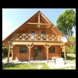 Dwupiętrowy drewniany dom z balkonem, świeżo po renowacji, z widoczną anteną satelitarną na dachu, otoczony zielonym trawnikiem i drzewami.