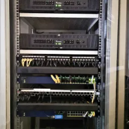 Szafa rack z zamontowanymi rejestratorami monitoringu wizyjnego, patch panelem i switchem sieciowym z podłączonymi przewodami Ethernet.