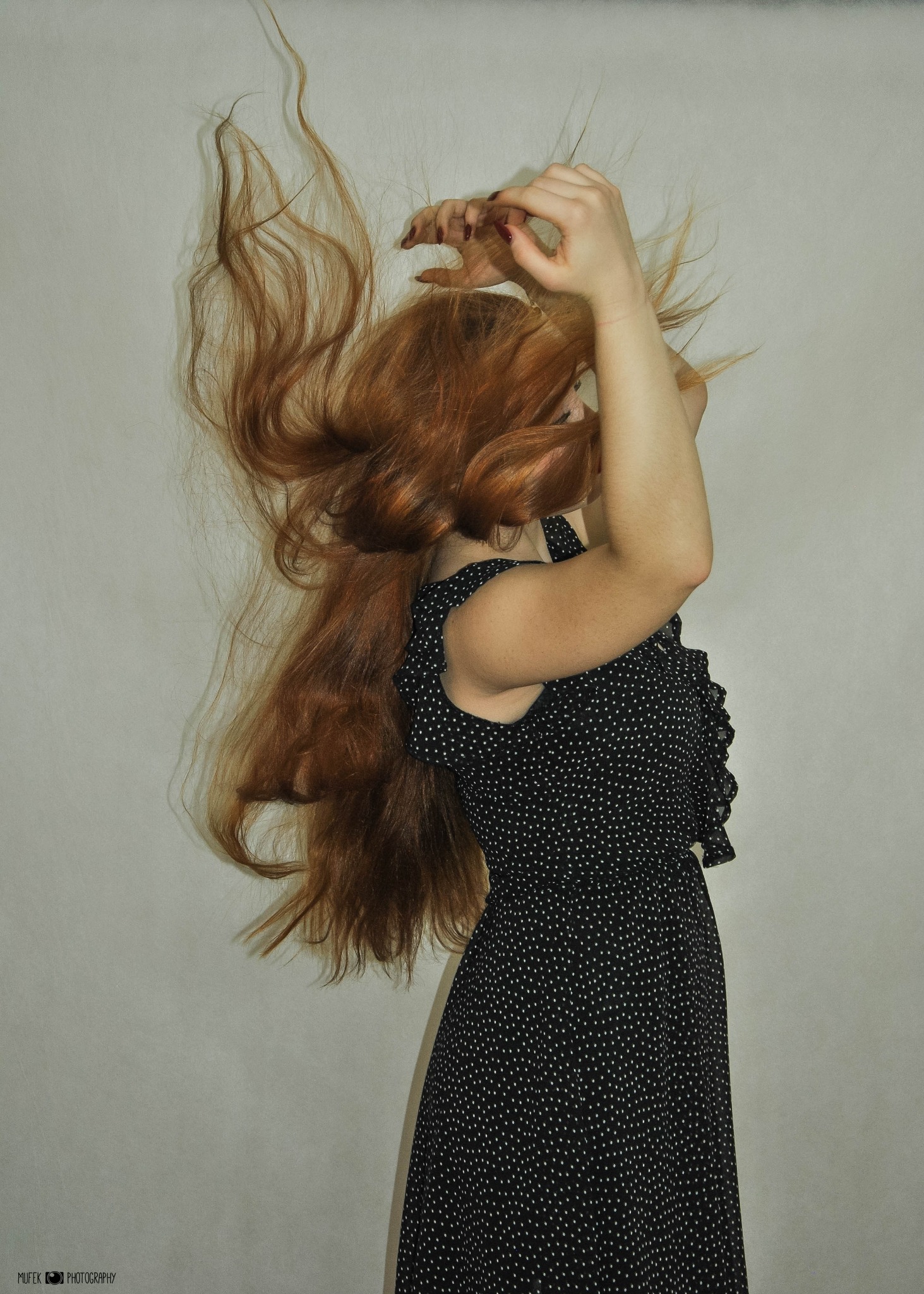 Rude włosy w ruchu: kobieta w czarnej sukience w białe kropki, dynamiczne ujęcie z uniesionymi rękami.