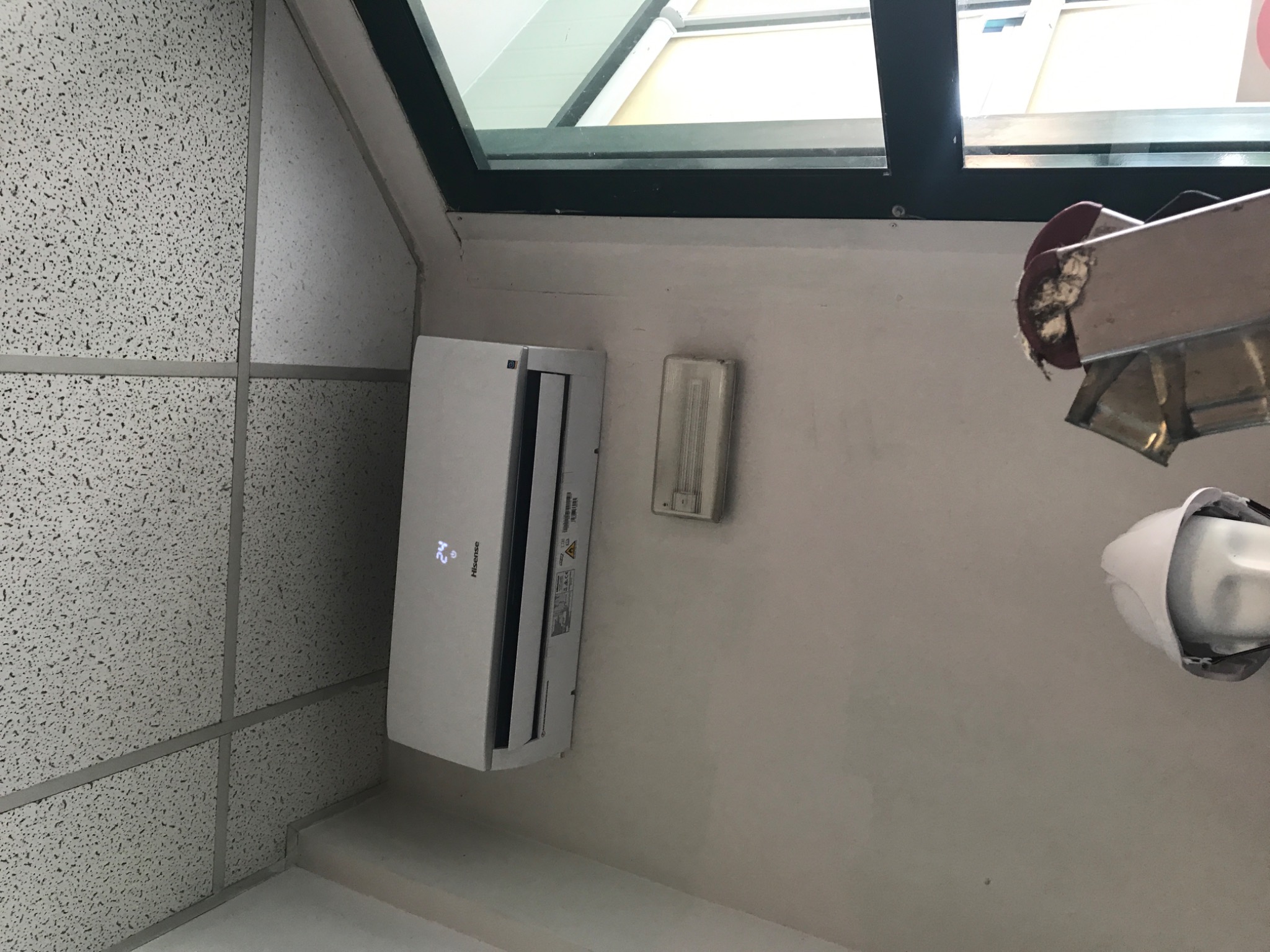 Biały klimatyzator ścienny marki Hisense zamontowany pod oknem, widoczny fragment drabiny z zabezpieczeniem na ścianie.