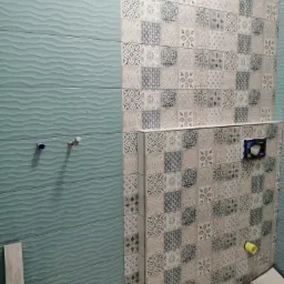 Łazienka w trakcie remontu: ściana wyłożona turkusowymi płytkami z falistym wzorem oraz dekoracyjnymi płytkami w odcieniach szarości i beżu, widoczne przyłącza hydrauliczne i instalacja podtynkowa.