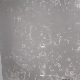 Szara ściana z efektem betonu architektonicznego, widoczne puszki elektryczne przed montażem osprzętu, nieregularna faktura z jaśniejszymi przetarciami.