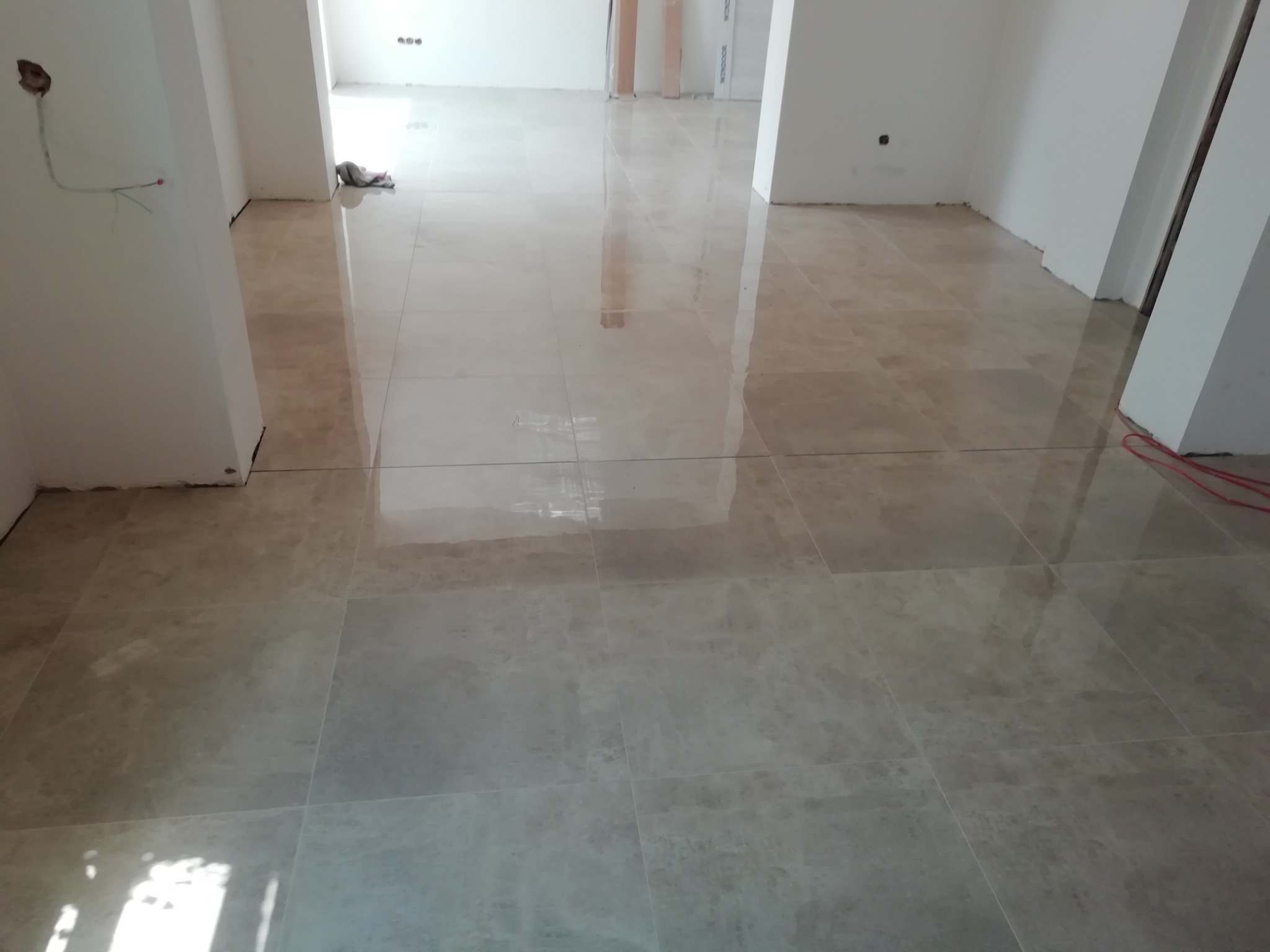 Wyłożona jasnobeżowymi płytkami podłoga w trakcie remontu, widoczne niedokończone ściany i wystające przewody elektryczne.