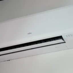 Biały klimatyzator Fujitsu zamontowany na ścianie, widoczne diody sygnalizujące pracę urządzenia.