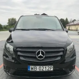 Przód czarnego Mercedesa Vito 116 z 2016 roku, wersja Long, z widoczną tablicą rejestracyjną WB 0212P i logo Mercedesa na tle szarej kostki brukowej.
