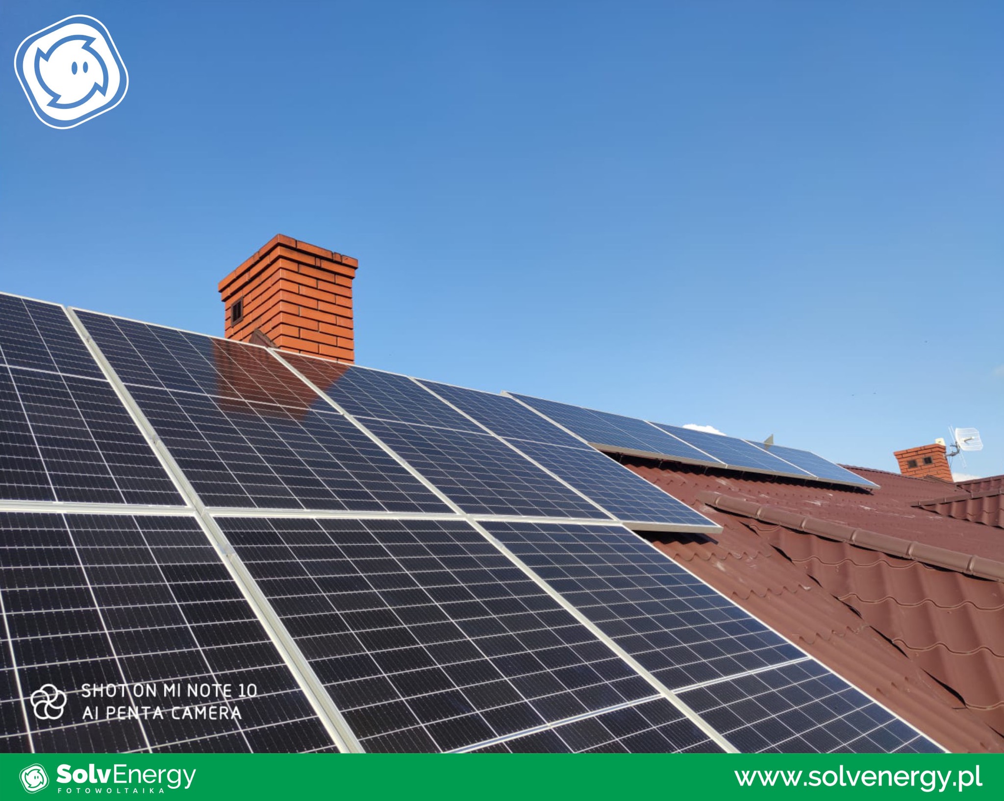 Panele słoneczne na brązowym dachu z ceglanym kominem w tle, widok z dołu pod kątem w słoneczny dzień.