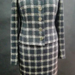 Damski komplet: krótka marynarka i spódnica, uszyte z ciemnej tkaniny w kratę z metaliczną nitką, zapinana na sześć okrągłych guzików, prezentowana na manekinie na ciemnym tle.