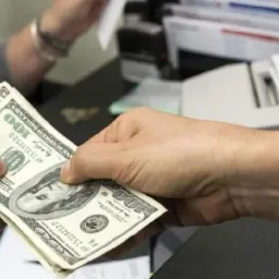 Wymiana banknotów 100 dolarowych między dwiema osobami przy biurku w banku.