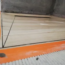 Fragment podłogi w trakcie układania płytek imitujących drewno, zabezpieczonych pomarańczową taśmą, widoczny fragment zaprawy.