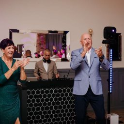 IvanTech Michał Iwanisik - Uśmiechnięci goście klaszczą podczas występu DJ-a, widoczne oświetlenie sceniczne i konsoleta DJ-ska z wzorem plastra miodu.