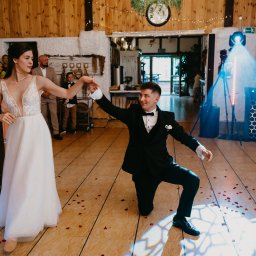 IvanTech Michał Iwanisik - Para młoda tańczy podczas wesela w Koszalinie, oświetlenie sceniczne, parkiet posypany płatkami róż, w tle wodzirej z mikrofonem.