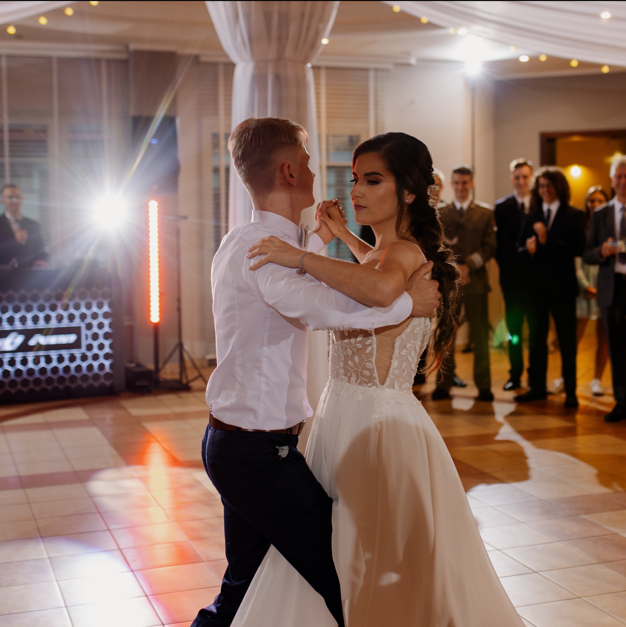 Para młoda w tańcu podczas wesela, oświetlenie sceniczne, goście w tle