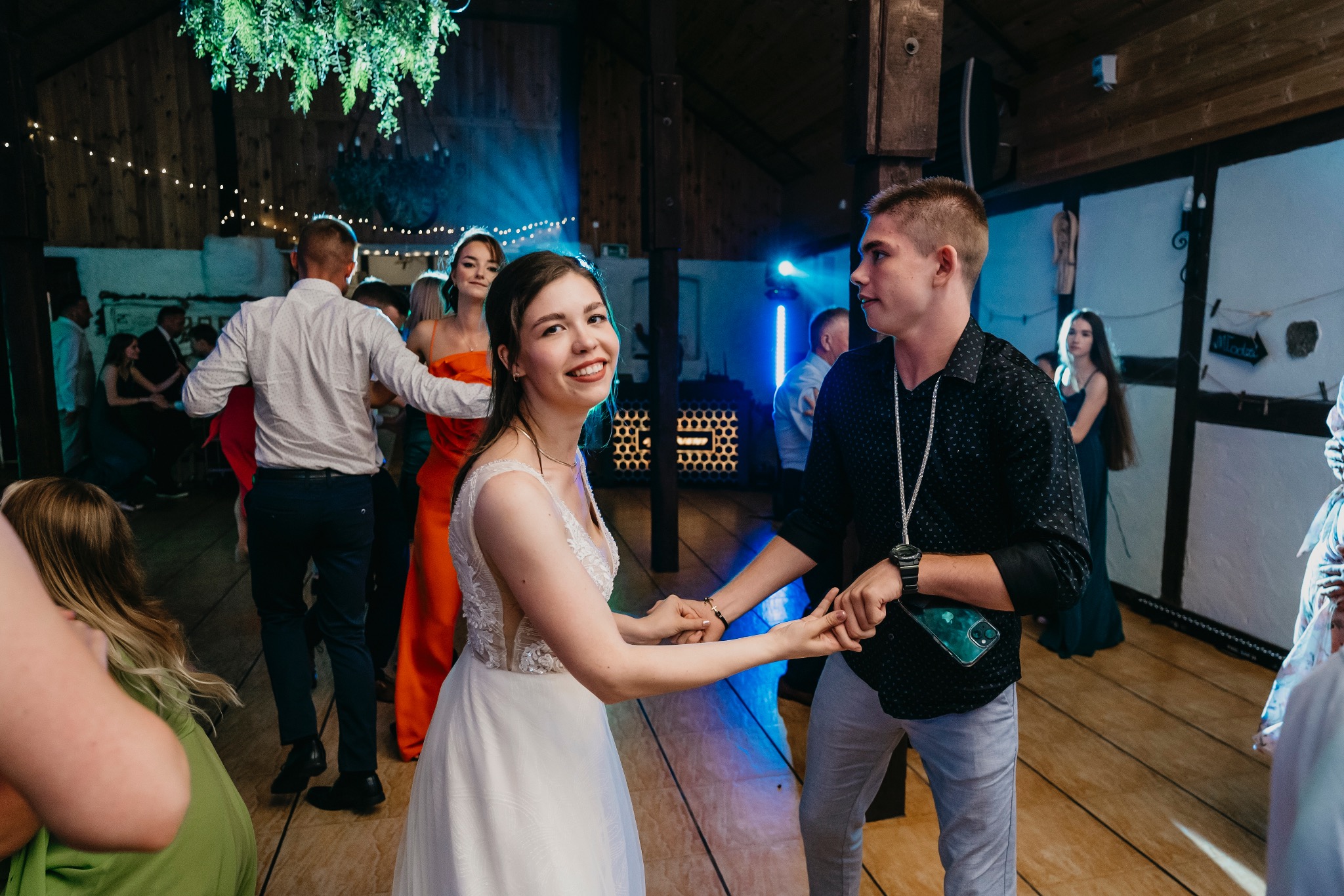 Para młoda tańczy na parkiecie podczas wesela, oświetlenie sceniczne w tle, dekoracja roślinna nad głowami.