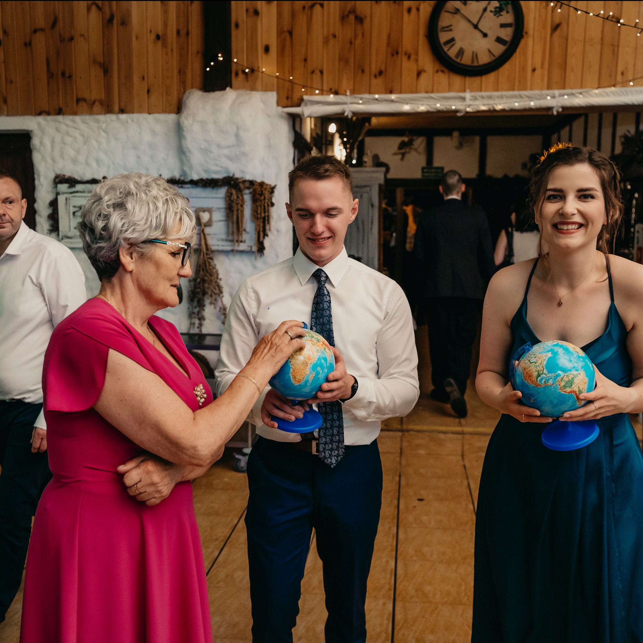 Goście weselni trzymają globusy jako element dekoracyjny lub atrakcję podczas przyjęcia, starsza kobieta dotyka globusa trzymanego przez młodego mężczyznę.