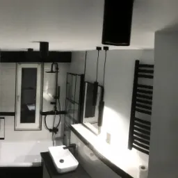 Nowoczesna łazienka w czerni i bieli z wiszącą umywalką, grzejnikiem drabinkowym i kabiną prysznicową za szybą, oświetlona wiszącymi lampami tubami.