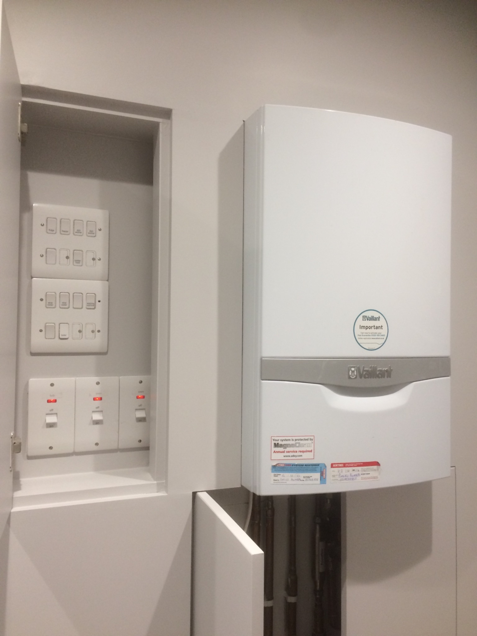 Nowoczesny, biały piec gazowy Vaillant zamontowany w łazience obok szafki z wyłącznikami elektrycznymi