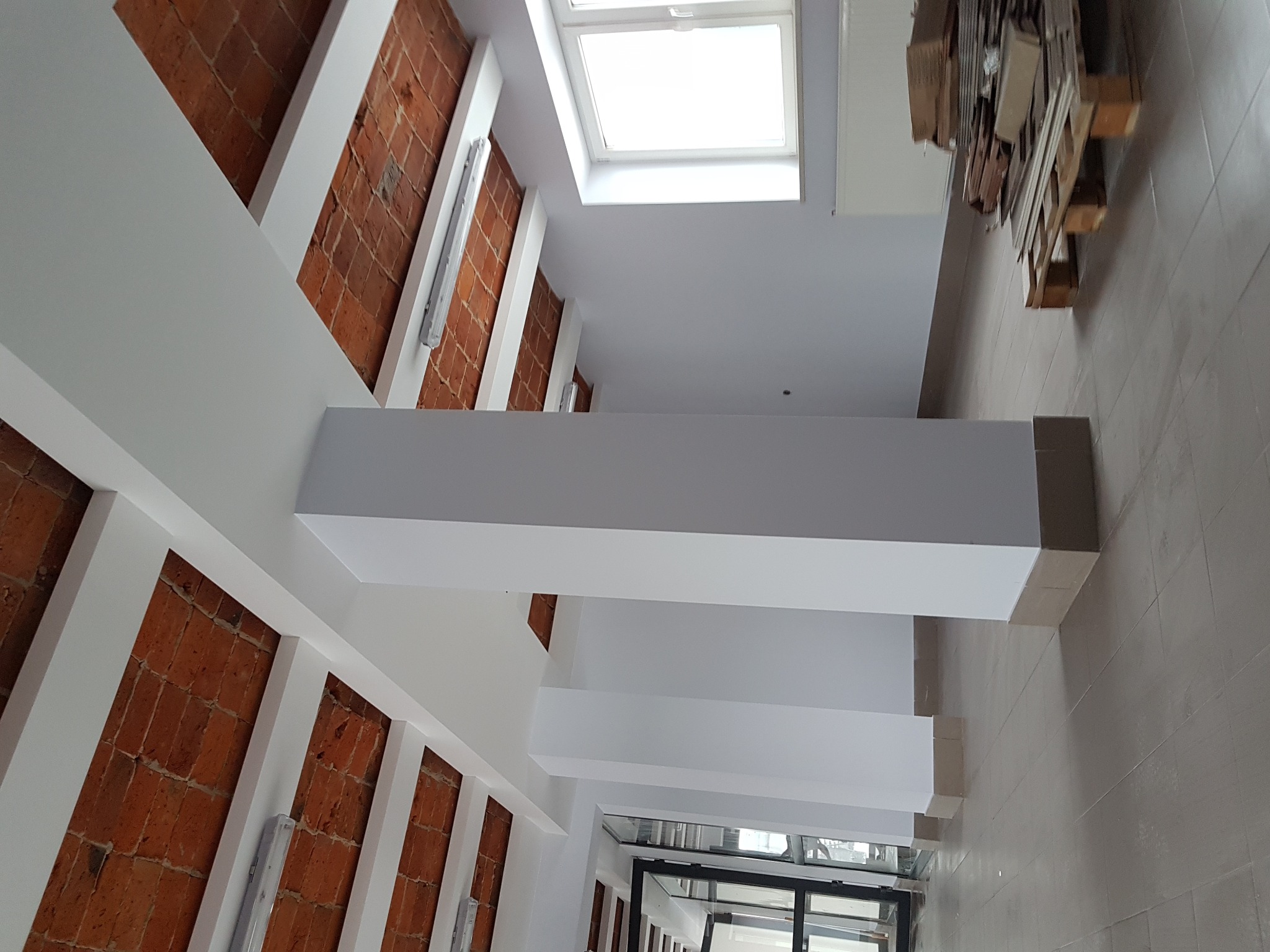 Korytarz z pomalowanymi na biało ścianami, fragmentami cegły i oknem dachowym, widok z dołu.