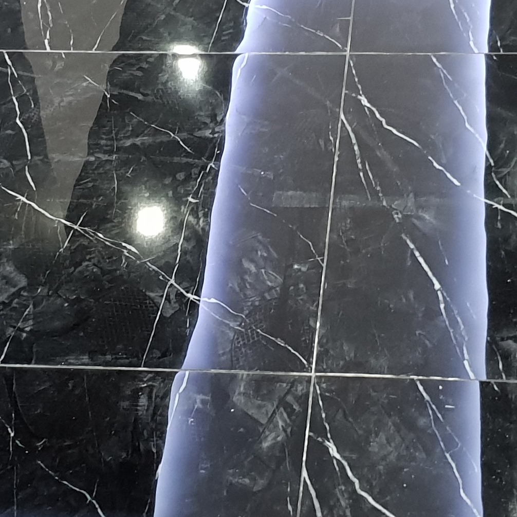 Położone, błyszczące, czarne płytki podłogowe z białym marmurkowym wzorem, częściowo oświetlone niebieskawym światłem.