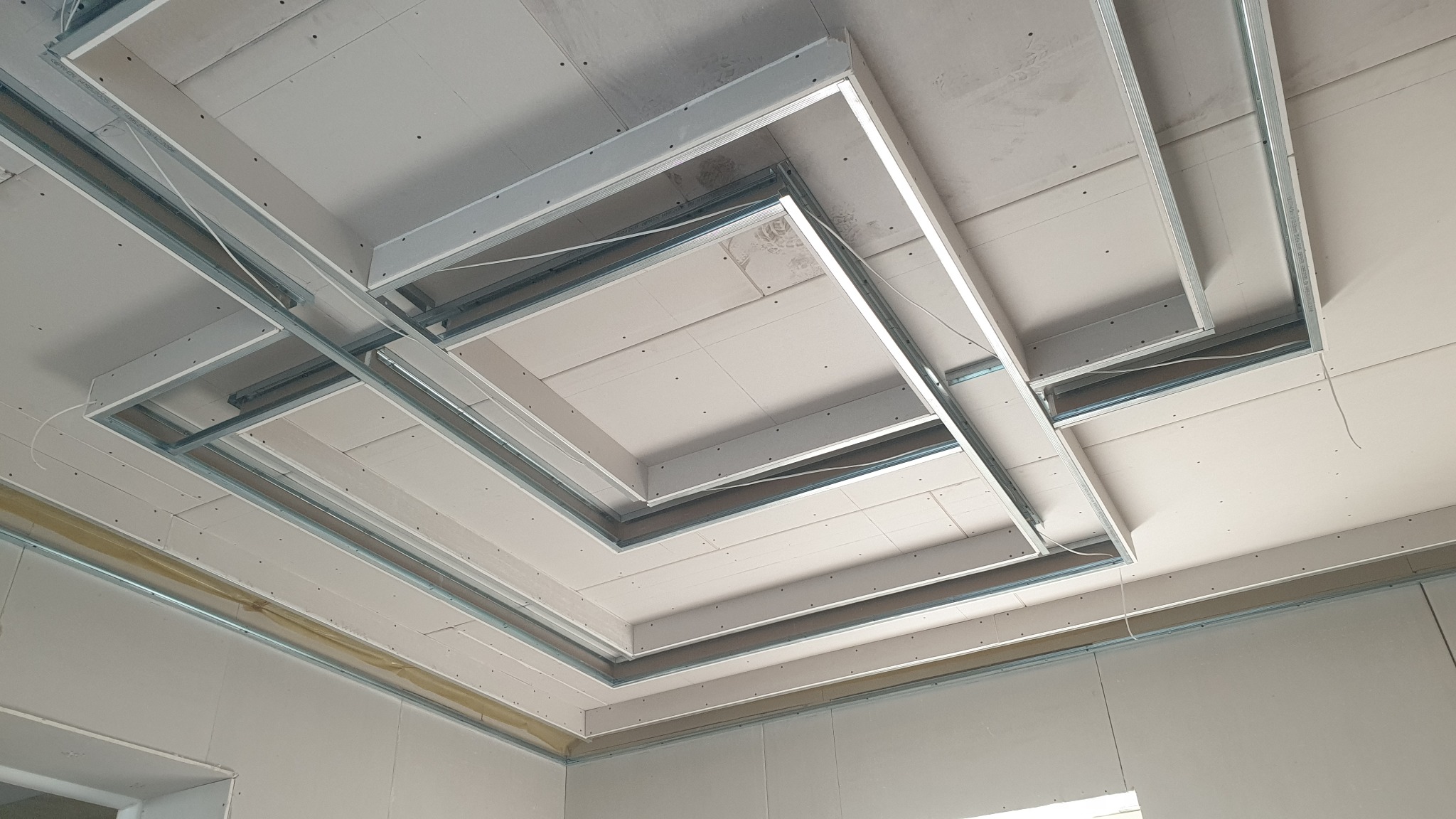 Sufit podwieszany z płyt gipsowo-kartonowych na metalowej konstrukcji, widoczne kable i niedokończone łączenia płyt