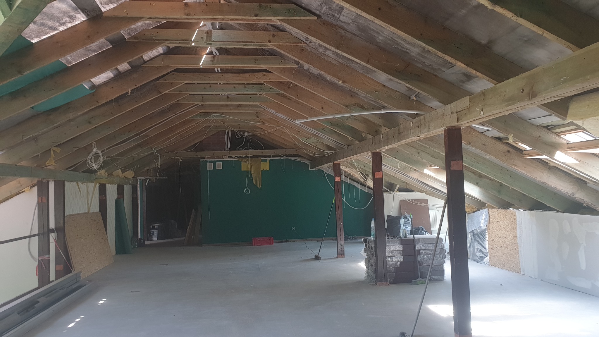 Poddasze w trakcie adaptacji: widoczne drewniane elementy konstrukcyjne dachu, ocieplenie wełną mineralną, instalacja elektryczna oraz fragmenty ścian z płyt gipsowo-kartonowych przed wykończeniem.