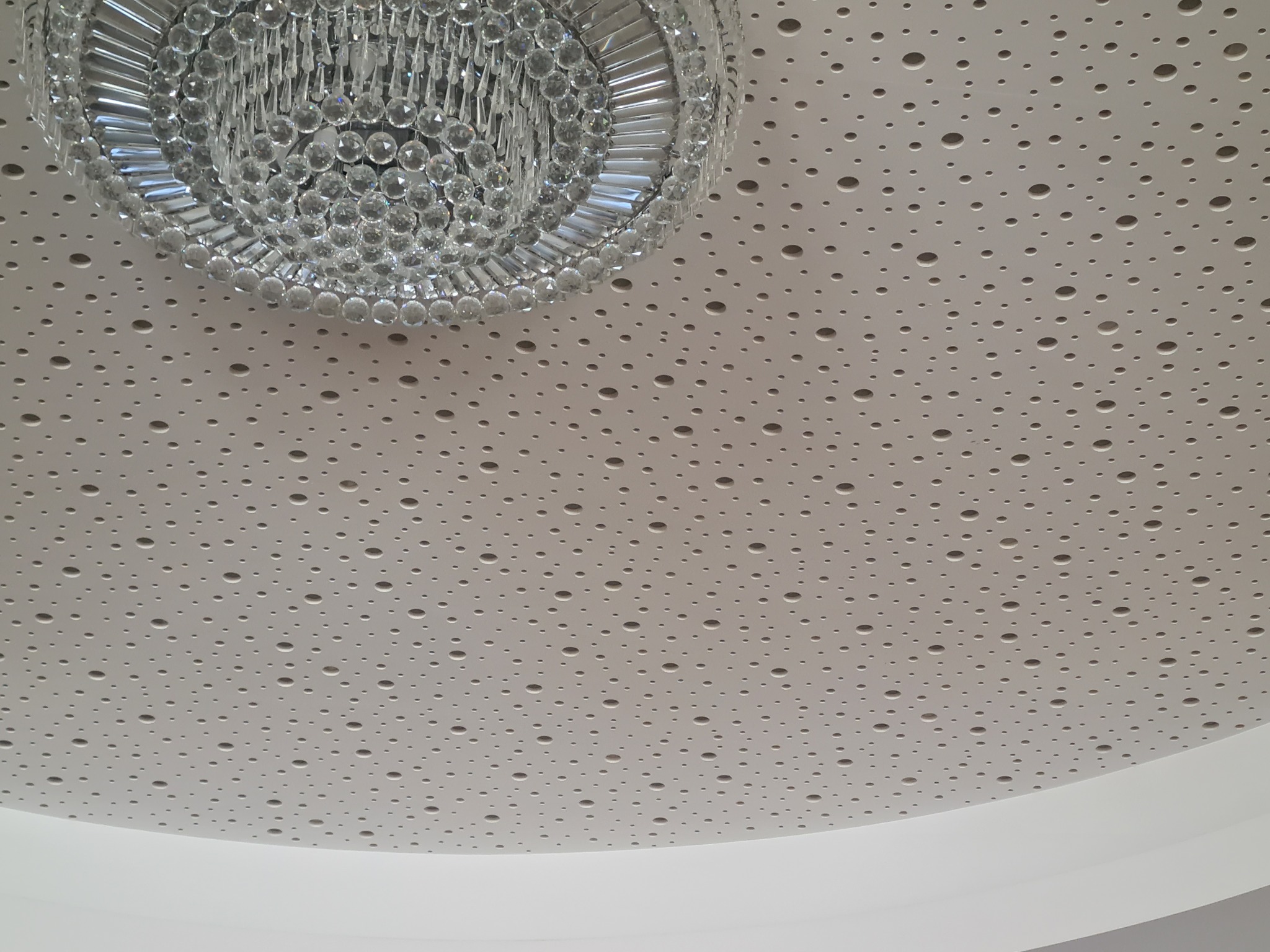 Dekoracyjny sufit podwieszany z perforacją i kryształowy żyrandol w nowoczesnym wnętrzu.