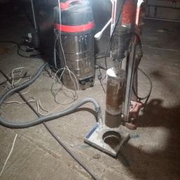 DEJV-BUD Cięcie i Wiercenie otworów w betonie, Technika Diamentowa - Wiertnica diamentowa rdzeniowa z odkurzaczem przemysłowym podczas wiercenia otworu w betonowej posadzce, widoczne ślady wody i urobku.