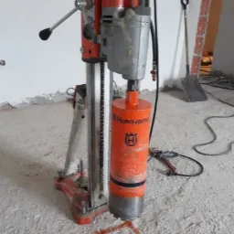 Wiertnica Husqvarna z wiertłem koronowym, przygotowana do wiercenia otworu w betonowej posadzce, zaznaczonego pomarańczowym kwadratem.