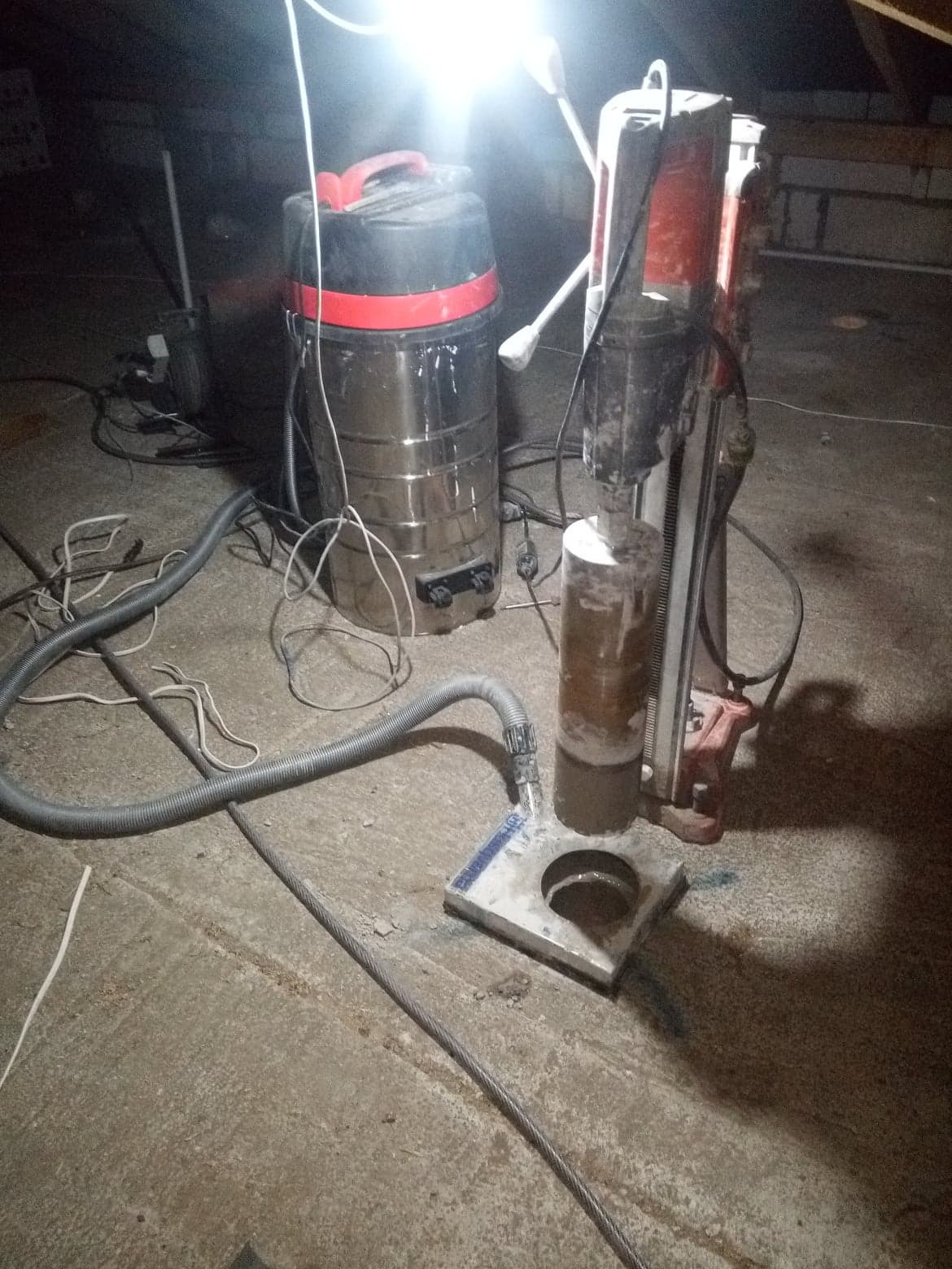 Wiertnica diamentowa rdzeniowa z odkurzaczem przemysłowym podczas wiercenia otworu w betonowej posadzce, widoczne ślady wody i urobku.