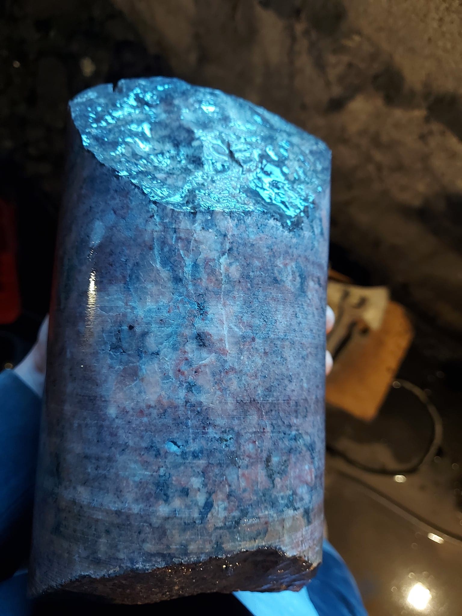 Rdzeń wiertniczy z widocznymi warstwami geologicznymi, mokry od wiercenia, trzymany w dłoni.